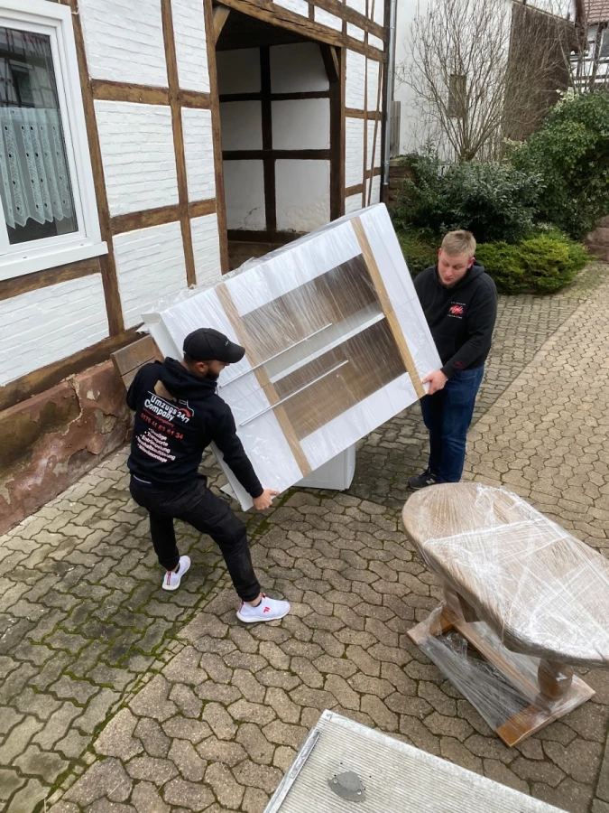 Umzugshelfer tragen verpackte Möbel an einem Haus